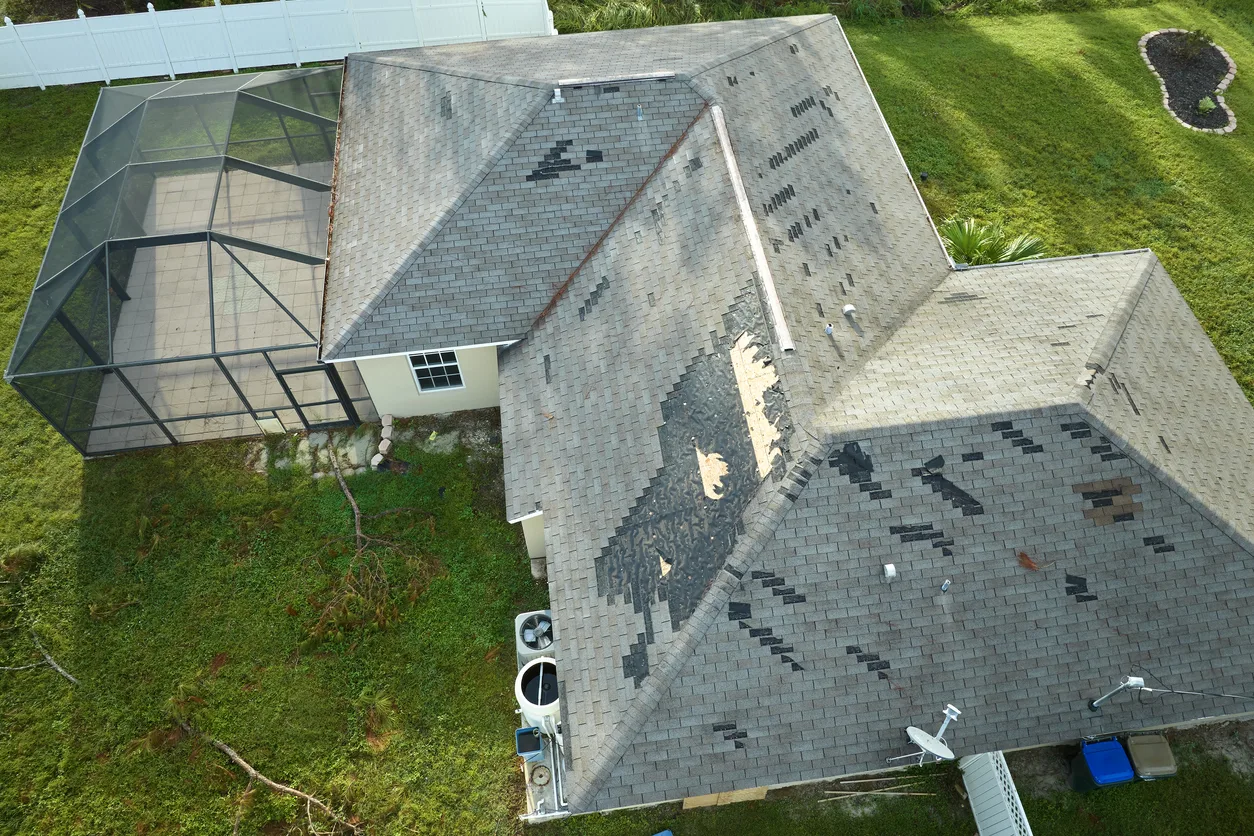 Wind damaged house roof with missing asphalt shingles after hurricane Ian in Florida. Repair of home rooftop concept