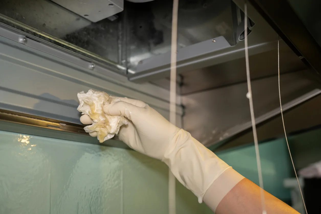 Someone hands using tissue paper to wipe a cooker hood for cleaning it.